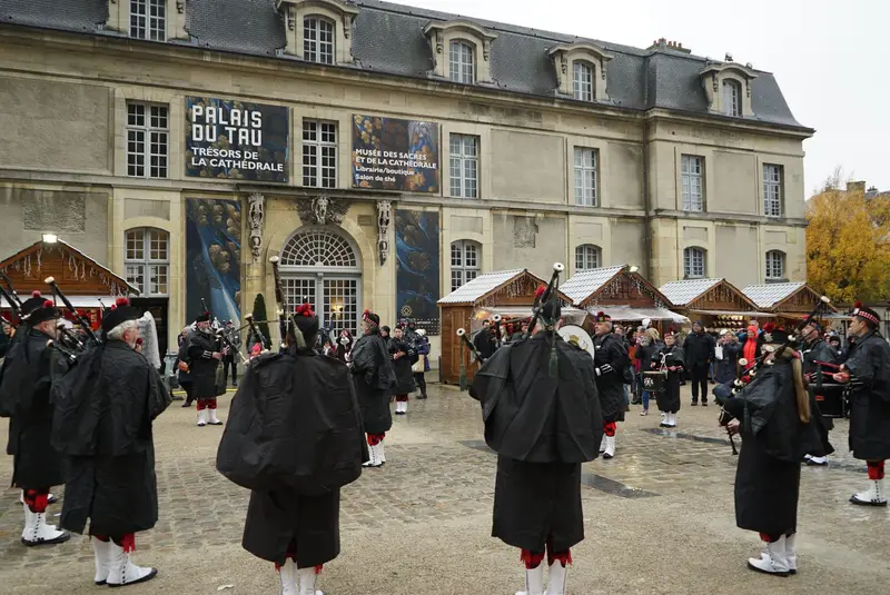 Chalets du marché de Noël de Reims devant le palais du Tau, avec des musiciens en costume